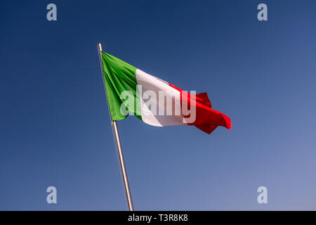 Basso angolo vista della bandiera dell'Italia agitando contro il cielo blu chiaro, pennone inclinato a sinistra Foto Stock