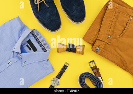 Abiti casual per abbigliamento uomo con la maglietta blu, senape jeans, cinghia, guarda, blu scarpe e accessori isolati su giallo, vista dall'alto. Foto Stock