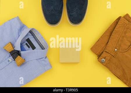 Abiti casual per abbigliamento uomo con la maglietta blu, senape jeans, cinghia, guarda, blu scarpe e accessori isolati su sfondo giallo, vista dall'alto Foto Stock