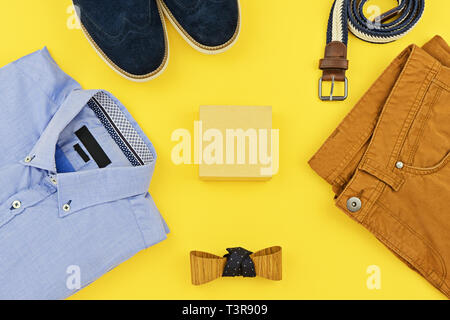 Abiti casual per abbigliamento uomo con la maglietta blu, senape jeans, cinghia, guarda, blu scarpe e accessori isolati su sfondo giallo, vista dall'alto Foto Stock