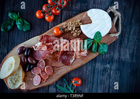 Il prosciutto, pane, olive, noci, mozzarella, salame, basilico e pomodori ciliegini marrone su tavola di legno. Cucina mediterranea. Vista dall'alto. Foto Stock