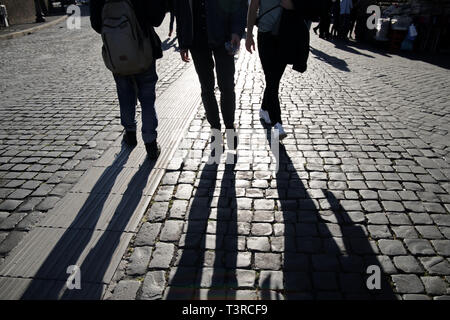 Sagome di camminare di più persone gambe sul terreno in ciottoli in controluce comprese le biciclette fotografato vicino al Vaticano a Roma Italia Foto Stock