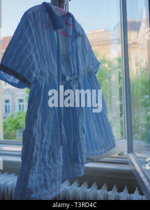 Una delle ragazze in blu estate shirt appesi per asciugare in finestra Foto Stock