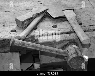 Gli antichi strumenti piccoli ax e grande martello sul vecchio banco in legno con una morsa e effetto bianco e nero Foto Stock