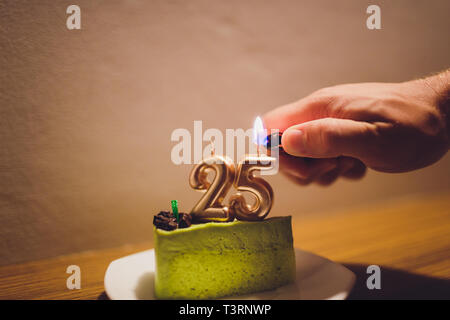 Venticinque anni di anniversario. Compleanno torta al cioccolato bianco con candele accese in forma di numero venticinque. Sfondo scuro con panno nero. Foto Stock