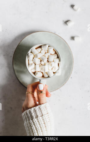 La mano della bambina detiene una tazza di cioccolata calda con marshmallow testurizzato su sfondo bianco. Vista superiore, piatto laici. Foto Stock