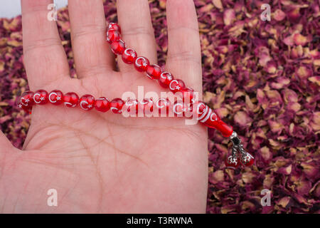 Perline in mano sul essiccati petali di rosa sullo sfondo Foto Stock