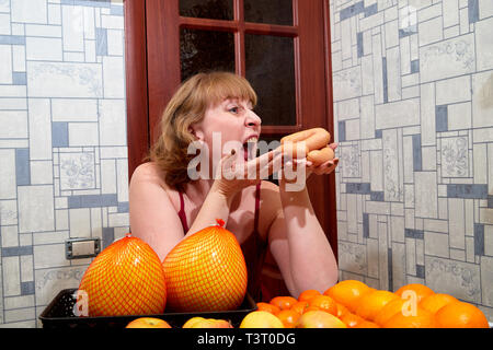 Donna di mezza età con frutta e salsicce a tavola in camera Foto Stock