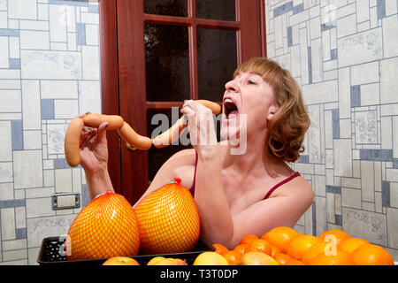 Donna di mezza età con frutta e salsicce a tavola in camera Foto Stock