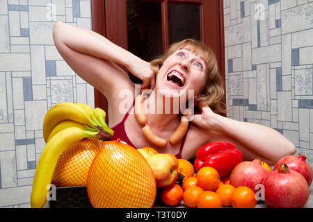 Donna di mezza età con frutta e salsicce a tavola in camera Foto Stock