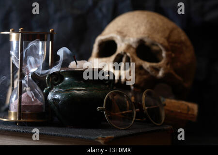 Scienza antica nozione. Cranio umano sul vecchio libro vicino a clessidra e candela Foto Stock