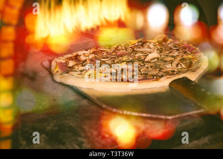 Freschi e originali della pizza italiana su una pala è messa in un tradizionale a legna forno di pietra. Foto Stock