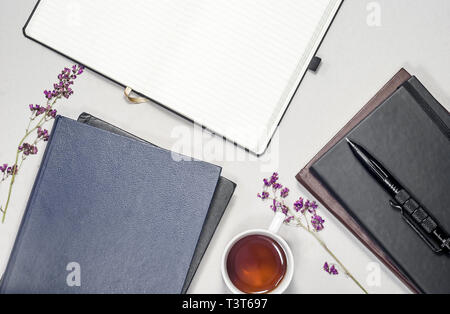 Composizione piana cup con tè, libri, pastiglie, penna, viola fiori secchi Foto Stock