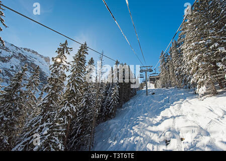 Vista panoramica di una coperta di neve catena montuosa alpina mentre si è in viaggio sulla seggiovia ski lift in presenza di luce solare Foto Stock