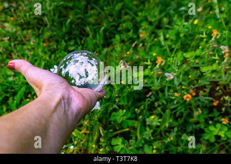 Donna di mano che regge una sfera di cristallo bianco con fiori di riflesso in esso close up Foto Stock