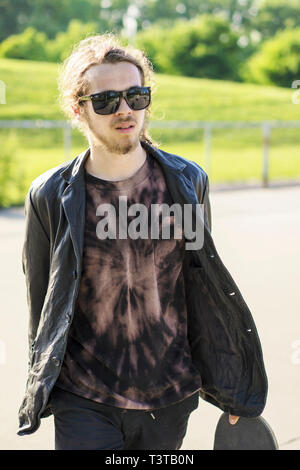 Uomo caucasico con la barba che trasportano skateboard Foto Stock