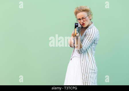 Ritratto di attenta funny giovane donna bionda in bianco striato blusa con occhiali in piedi tenendo la chitarra elettrica, cercando e concentrandosi sulla venuta Foto Stock