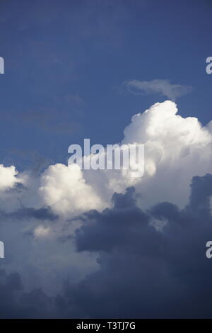 Nuvole stratificato, lanuginoso bianco e grigio scuro, nella parte anteriore del cielo blu Foto Stock