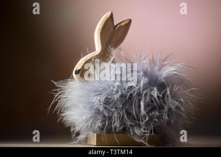 Legno coniglietto di pasqua con piume grigie. In studio illuminato bunny figura in gradiente di colore rosa. Spazio di copia e la struttura chiara. Foto Stock