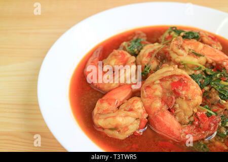 Piastra di stile thai piccante di mescolare i gamberi fritti con santo basilico servito su un tavolo di legno Foto Stock