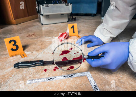 La polizia di esperti esamina con lente di ingrandimento un coltello con il sangue sulla scena di un crimine, immagine concettuale Foto Stock