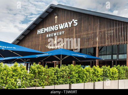 Cairns, Australia - 17 Febbraio 2019: Marrone edificio in legno di Hemingway's Brewery sul pontile. Il fogliame verde e blu tabella ombrelloni. Foto Stock