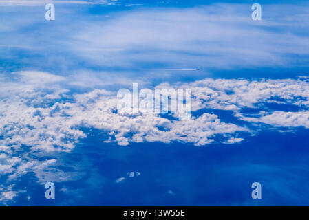 Intenso il cielo blu con nuvole bianche ed il piano che la attraversano, visto da sopra in un altro piano. Foto Stock