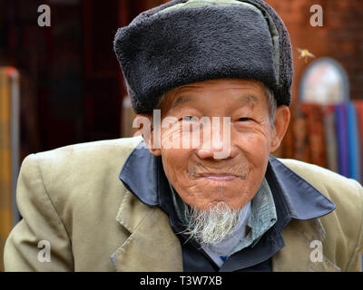 Vecchio fiume cinese fisherman indossa un militare-style ushanka hat e sorrisi per la fotocamera. Foto Stock