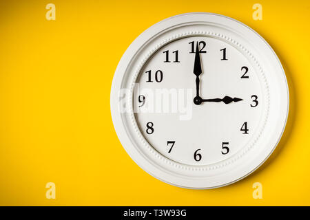 Grande orologio bianco appeso a una parete di colore giallo Foto Stock