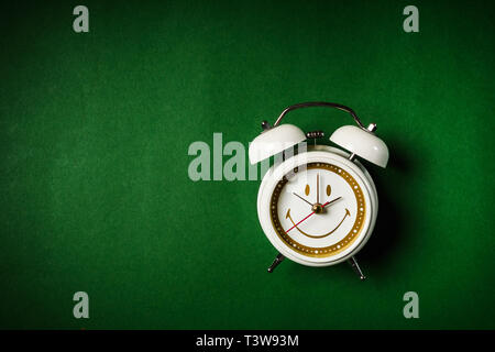 Piccolo orologio bianco posto su uno sfondo verde Foto Stock