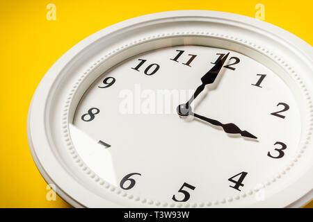 Grande orologio bianco appeso a una parete di colore giallo Foto Stock