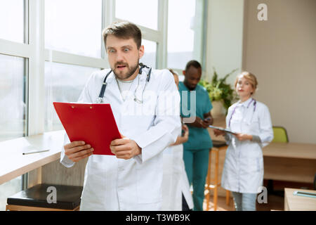 Bella sorpresa maschio medico professionale in piedi sopra lo sfondo dell'ospedale. L'immagine pubblicitaria sulla sanità, salute, clinica, medicina. Foto Stock