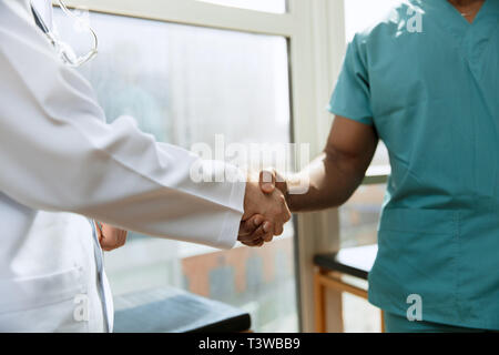 Trattativa. Concetto di collaborazione nel campo della medicina. Close up foto di due medici stringono le mani sul grigio Sfondo dell'ospedale. L'immagine pubblicitaria sulla sanità, salute, clinica, medicina e lavoro di squadra. Foto Stock