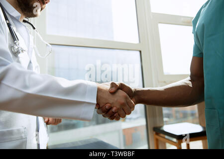 Trattativa. Concetto di collaborazione nel campo della medicina. Close up foto di due medici stringono le mani sul grigio Sfondo dell'ospedale. L'immagine pubblicitaria sulla sanità, salute, clinica, medicina e lavoro di squadra. Foto Stock