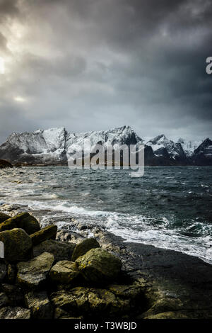 Montagne innevate affacciato sulla costa rocciosa, la Reine, Isole Lofoten in Norvegia Foto Stock