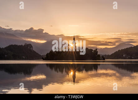Alba sul campanile di una chiesa riflessa in ancora sul lago di Bled, Alta Carniola, Slovenia Foto Stock