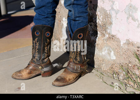 Vecchio stivali da cowboy sono alterate e marrone con design cucita sul lato con propaggini indossata da un vecchio cowboy in jeans. Foto Stock