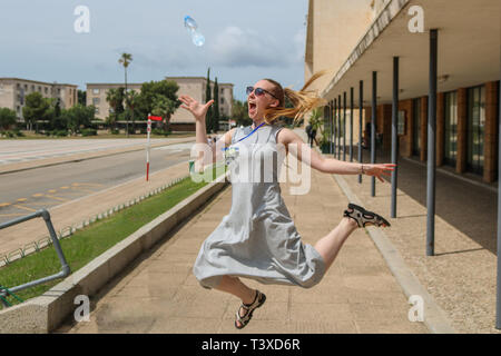 Ragazza bionda jumping, la cattura di una bottiglia di acqua Foto Stock