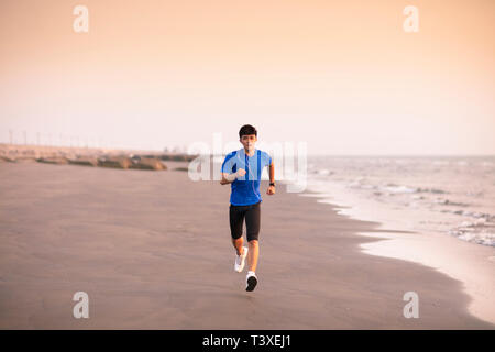 Giovane uomo che corre sulla spiaggia al tramonto Foto Stock