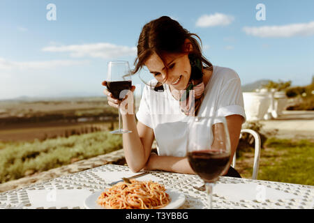 Donna sorridente seduti a tavola in un ristorante a cielo aperto con un vigneto in background. Donna sorridente su un vino data udienza con un bicchiere di r Foto Stock