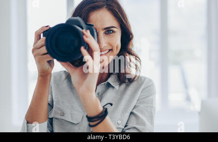 Donna con fotocamera DSLR a fotografare in interni di prendere alcune foto. Felice fotografo femmina a scattare foto con la fotocamera professionale. Foto Stock