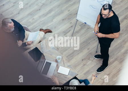 Imprenditore maturo presentando le sue idee sulla lavagna per i colleghi. Manager dando la presentazione per il suo team in sala conferenze presso l'ufficio. Foto Stock