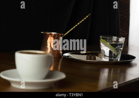 Un bicchiere di caffè con caffè e cioccolato accanto a un caffè con il latte in una tazza bianca collocato su un tavolo marrone Foto Stock