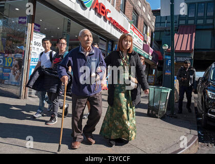 Una giovane donna asiatica va a braccetto con un uomo più anziano, presumibilmente il suo nonno. Su 74a san in Jackson Heights, Queens, a New York City. Foto Stock