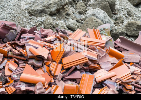 Incrinati tegola di tetto. Cumulo di macerie. Costruzione di discarica di rifiuti dettaglio. Pila di rotture di pezzi in ceramica e sfocata detriti di cemento in background. Rovine di colore rosso. Ecologia. Foto Stock