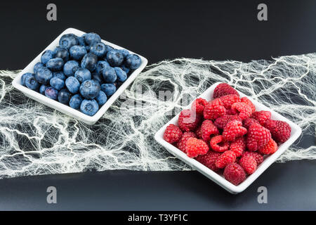 Una sana frutta di bosco. Il lampone rosso e blu di mirtilli. Sfondo nero. Dolci fresche bacche succosa. Quadrato bianco a bocce. Decorativa tessile fibroso. Foto Stock