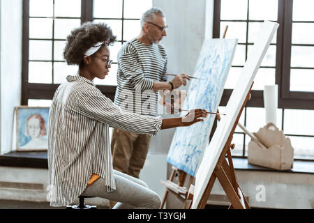 Lavorando in prossimità di insegnante. Talento promettente artista femminile sentirsi responsabili mentre si lavora vicino al suo insegnante Foto Stock