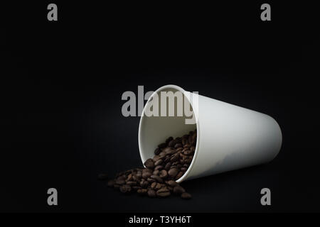 Carta tazza da caffè con schizzi di caffè in grani, sfondo nero. Chicchi di caffè tostati. Foto Stock