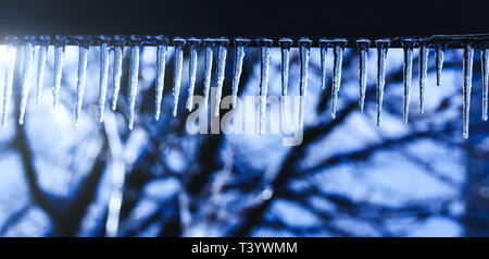 Magic crystal ghiaccioli pendenti dal tetto. Icicle di fusione con la caduta di gocce lucido su un bellissimo sfondo luminoso. Stalattiti di ghiaccio nel freddo inverno Foto Stock