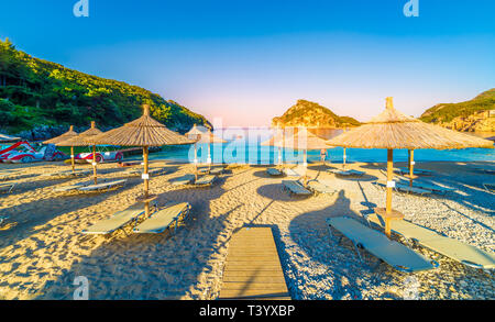 Spiaggia, sedie a sdraio e ombrelloni presso sunrise a Paleokastritsa village, l'isola di Corfù, Grecia Foto Stock